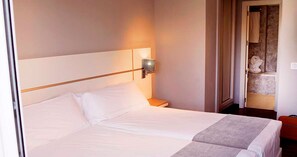 A hotel room with a large bed, a nightstand, a wall-mounted lamp, and a bathroom visible through an open door. - Hotel Vertice Chipiona Mar (Chipiona)