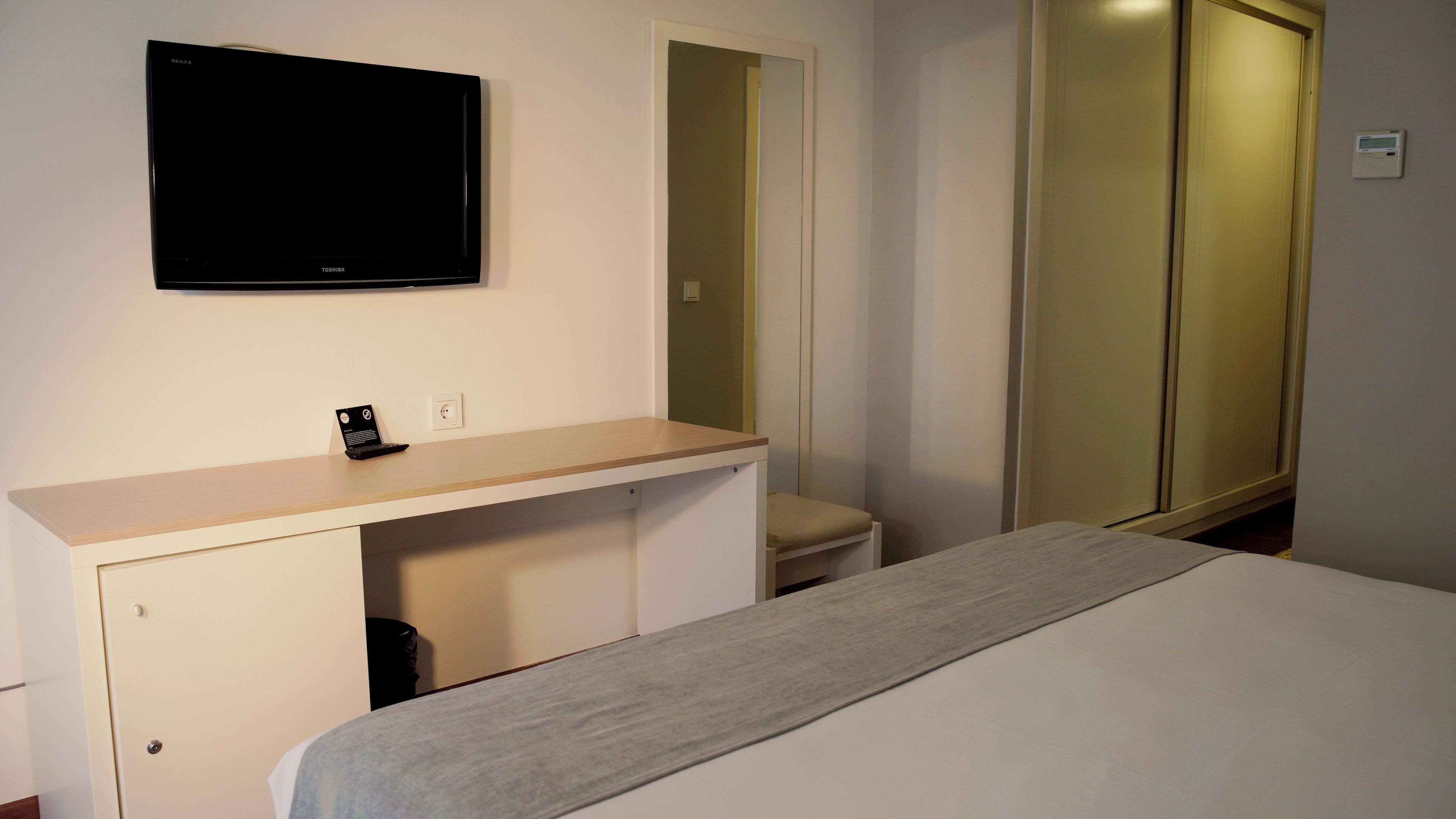 A hotel room with a bed, a desk with a laptop, a TV, and a wardrobe.
