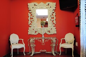 A room with a red wall, a white ornate mirror, and two white chairs. - Hotel Vertice Chipiona Mar (Chipiona)