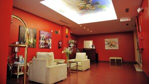 Um saguão de hotel com paredes vermelhas, um balcão de recepção e um claraboia no teto.