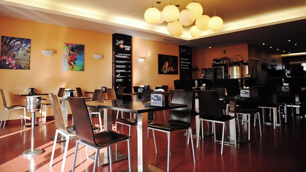 A restaurant with tables and chairs, a menu board, and a ceiling light fixture. - Hotel Vertice Chipiona Mar (Chipiona)