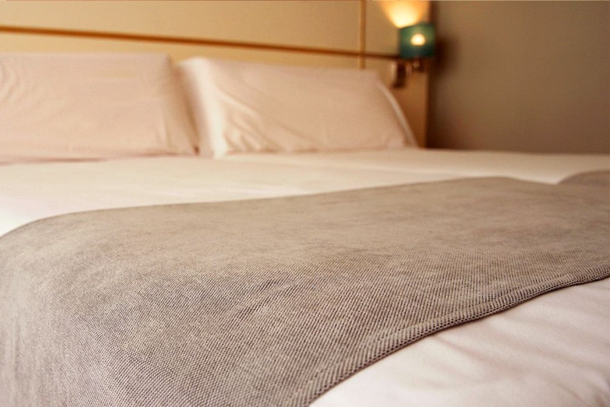 A neatly made bed with white linens and a beige throw blanket.