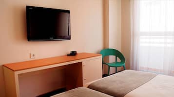 Habitación de hotel con una cama, un escritorio con computadora, una silla verde y un televisor montado en la pared.