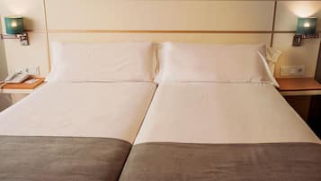 Una cama doble con sábanas blancas, dos mesitas de noche, un teléfono y lámparas de pared.