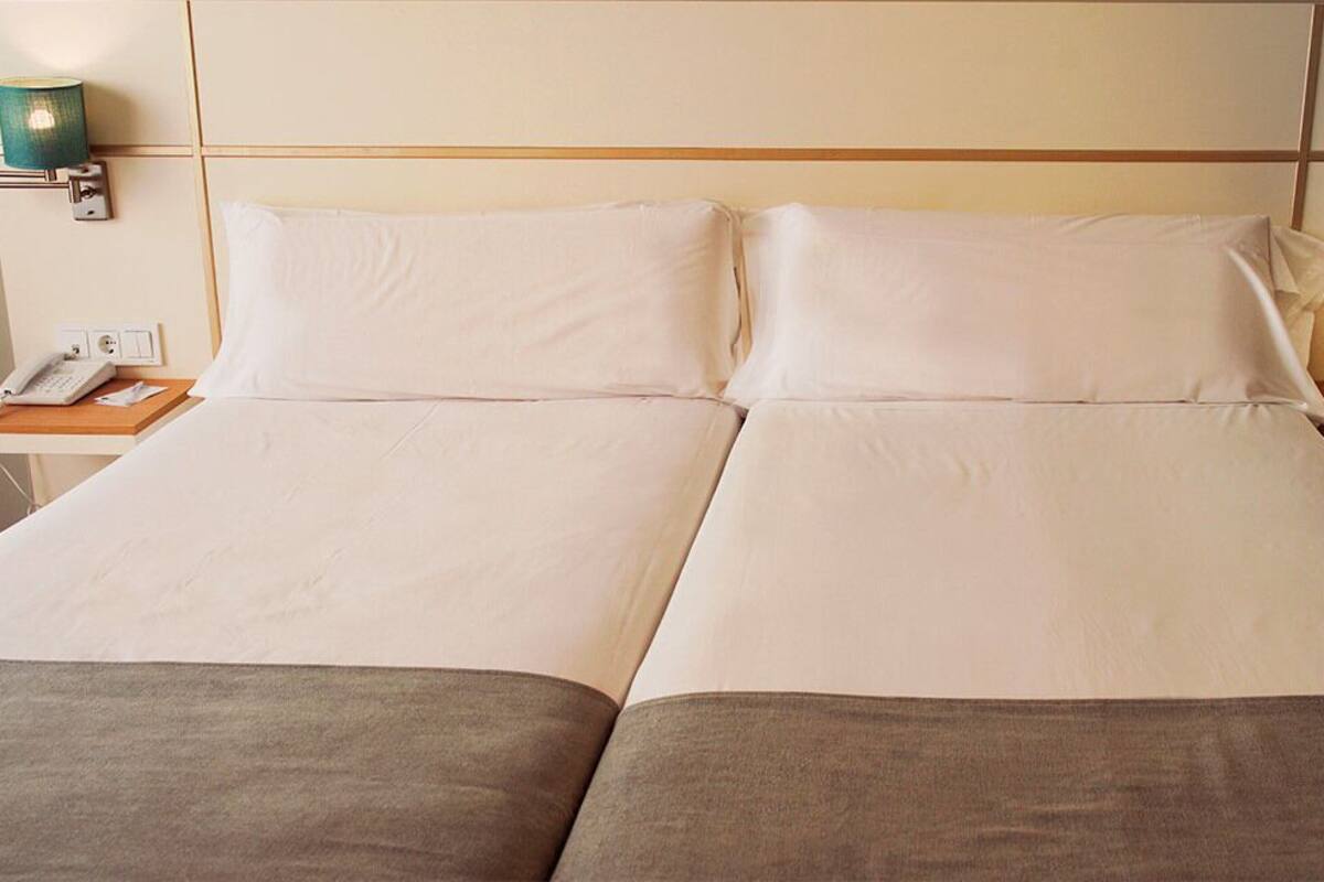 A double bed with white linens, two bedside tables, a phone, and wall-mounted lamps.