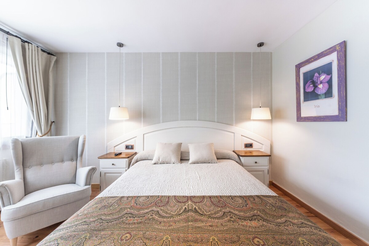 Quarto com cama grande, duas mesas de cabeceira, uma cadeira e um quadro na parede.