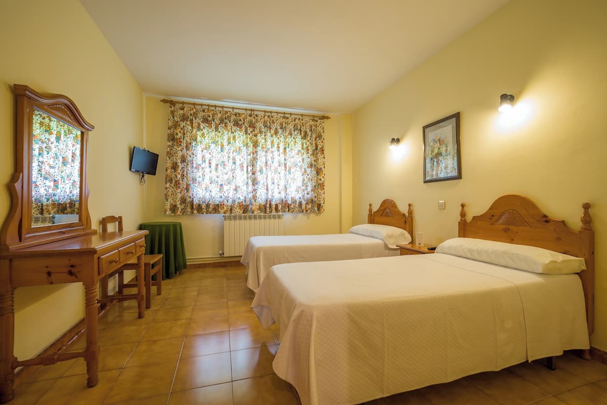 A room with two beds, a desk, a chair, a radiator, a television, and a window with curtains.