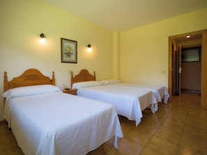 A hotel room with two single beds, a wooden headboard, a nightstand, a painting on the wall, and a door leading to another room. - El Mirador (Puertolas)