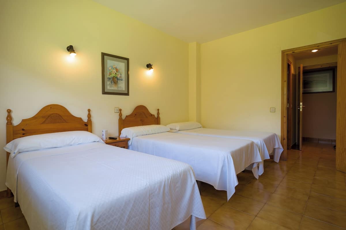 A hotel room with two single beds, a wooden headboard, a nightstand, a painting on the wall, and a door leading to another room.