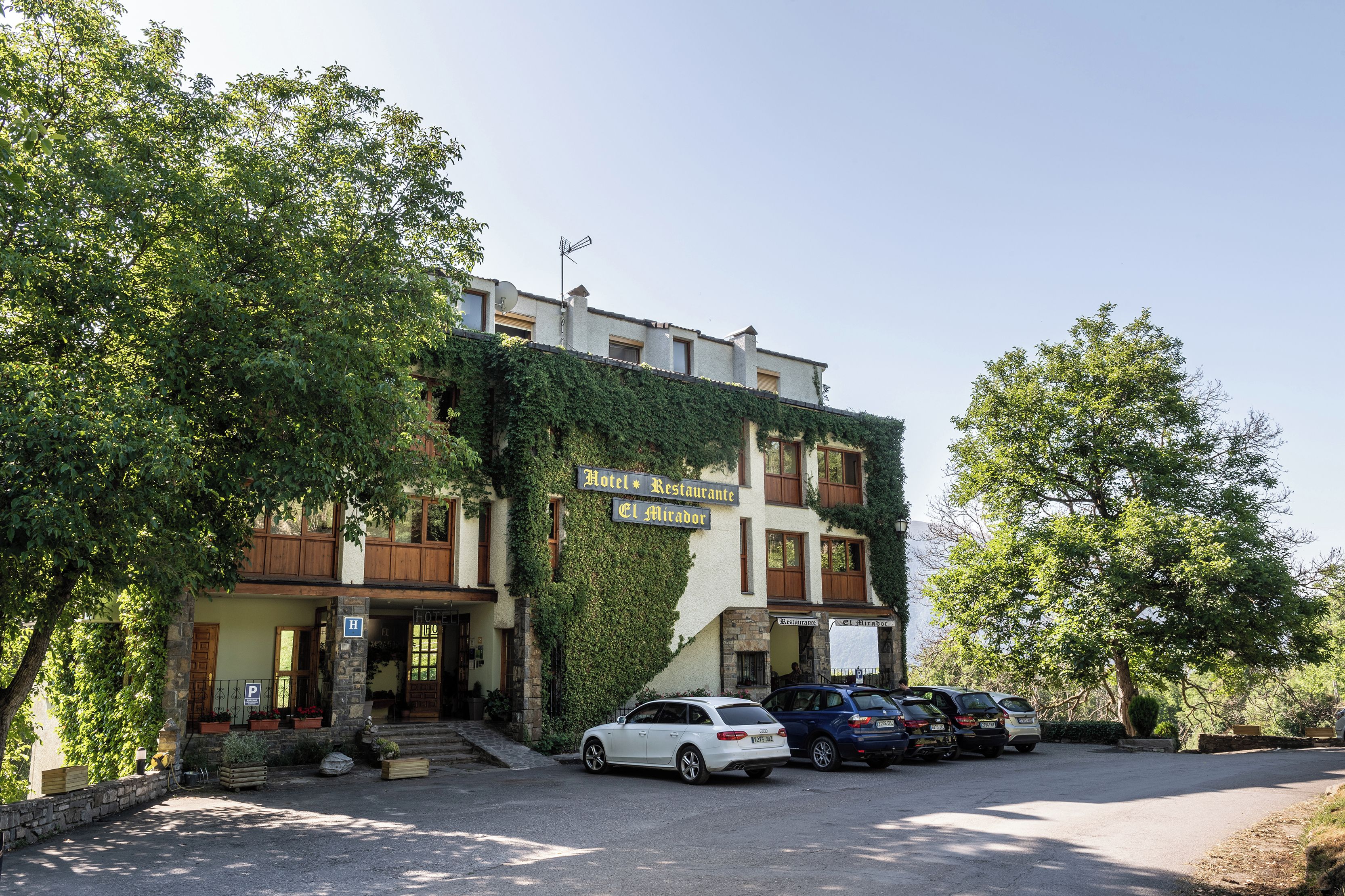Un hotel amb un rètol que diu "Hotel Restaurante El Mirador" i una zona d'aparcament amb diversos cotxes.
