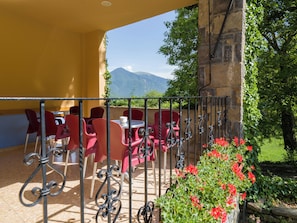 Une terrasse avec des chaises et des tables rouges, un mur en pierre et une vue sur les montagnes.