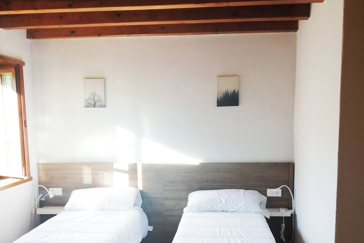 Una stanza con due letti, pavimento in legno e soffitto a falde.