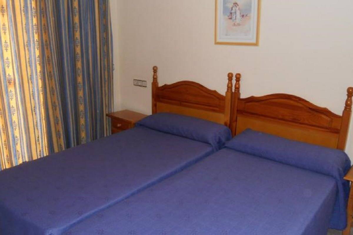 A double bed with a wooden headboard, two bedside tables, and a curtain with a striped pattern.