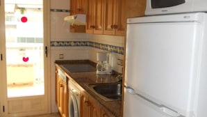 Una cocina con armarios de madera, un refrigerador blanco, una cafetera y una lavadora.