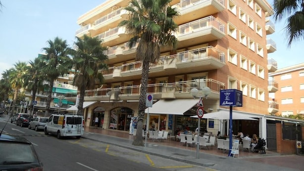 Un hotel de varios pisos con balcones, palmeras y zonas de estar al aire libre.