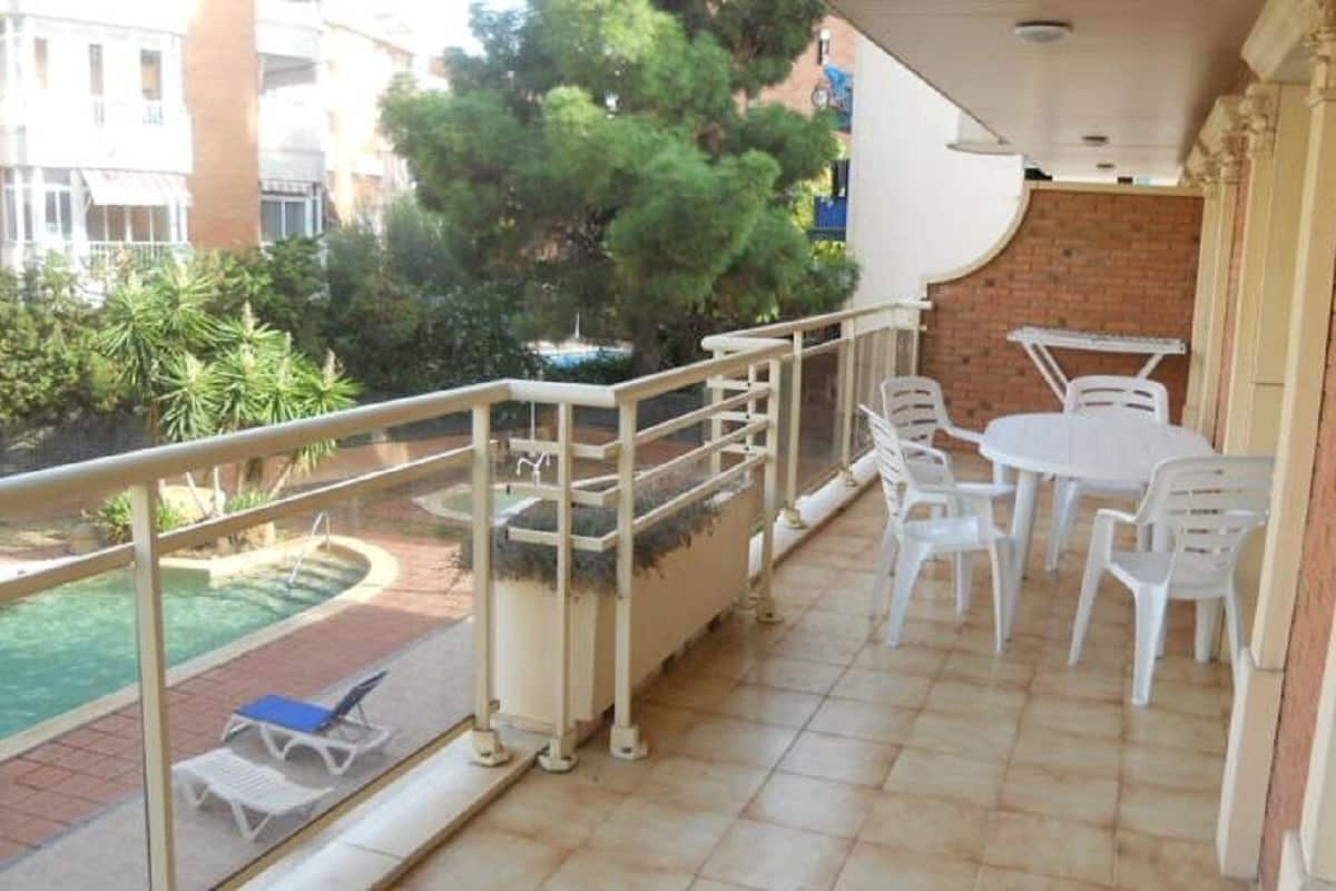 A balcony with a pool, white plastic chairs, and a table.