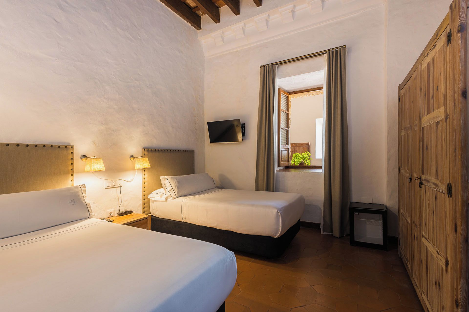 A hotel room with two beds, a television, a small table, and a wardrobe.