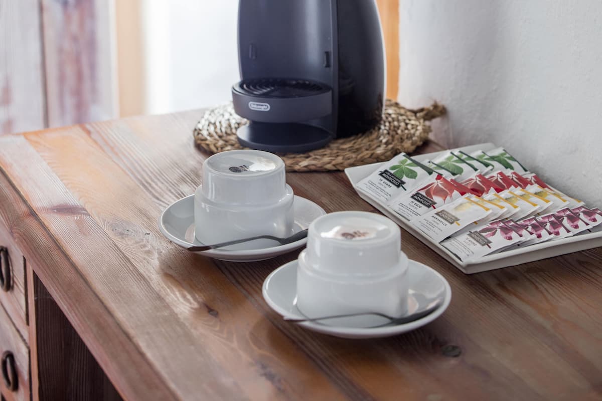 Eine Kaffeemaschine auf einem Holztisch mit zwei weißen Tassen und Untertassen, einer gewobenen Tischmatte und einer Speisekarte.