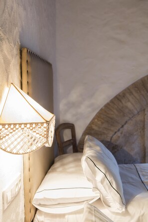 Een slaapkamer met een hoofdeinde, een bedlampje, een bed met kussens en een stoel.