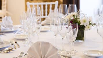 Mesa de comedor formal cubierta con mantel blanco, cubiertos y copas de vino, con un jarrón de flores en el centro.