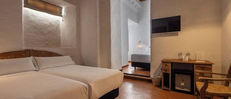 Quarto com cama, escrivaninha, cadeira, televisão e luminária pendente.