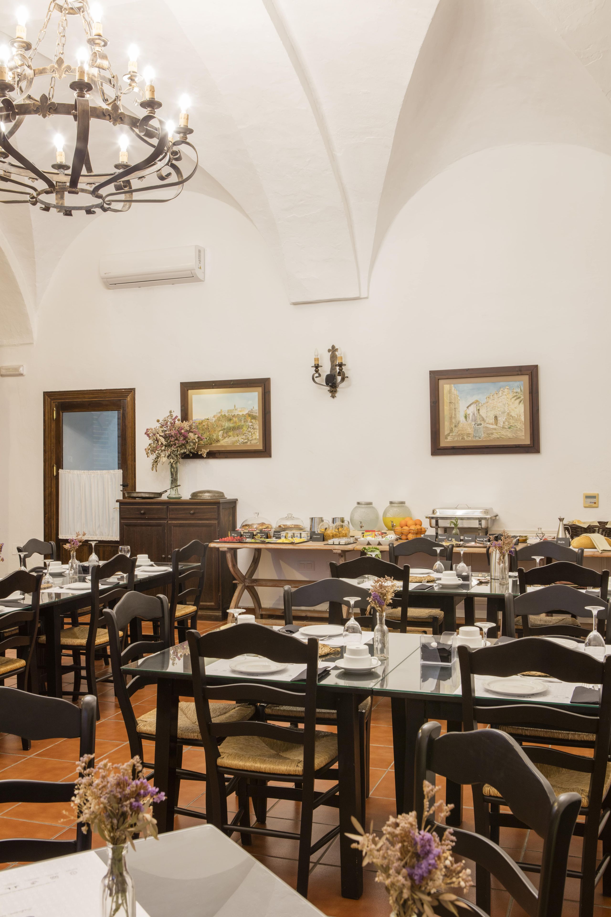 A dining area with tables set for meals, a chandelier, and artwork on the walls.