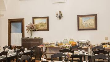 A dining area with tables set for meals, a chandelier, and artwork on the walls.
