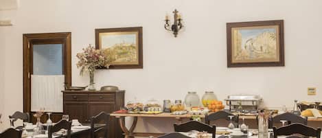 A dining area with tables set for meals, a chandelier, and artwork on the walls.