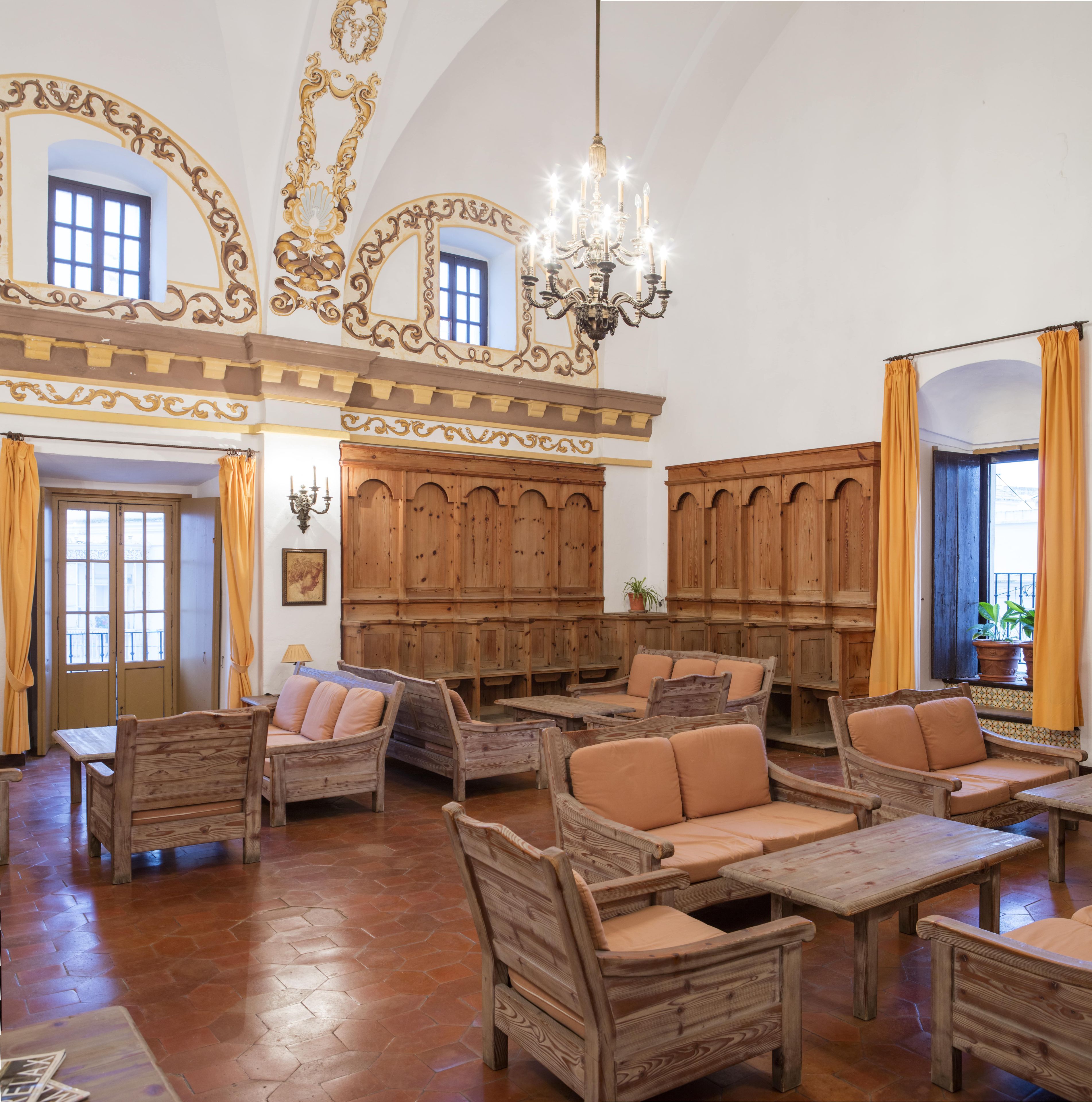 A spacious room with wooden furniture, a chandelier, and large windows with curtains.