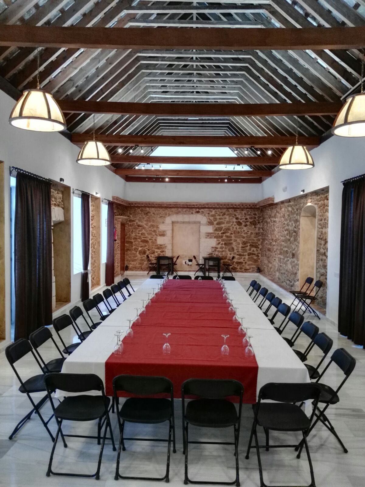 Un salón de conferencias con una mesa larga, sillas negras y una pared de piedra.