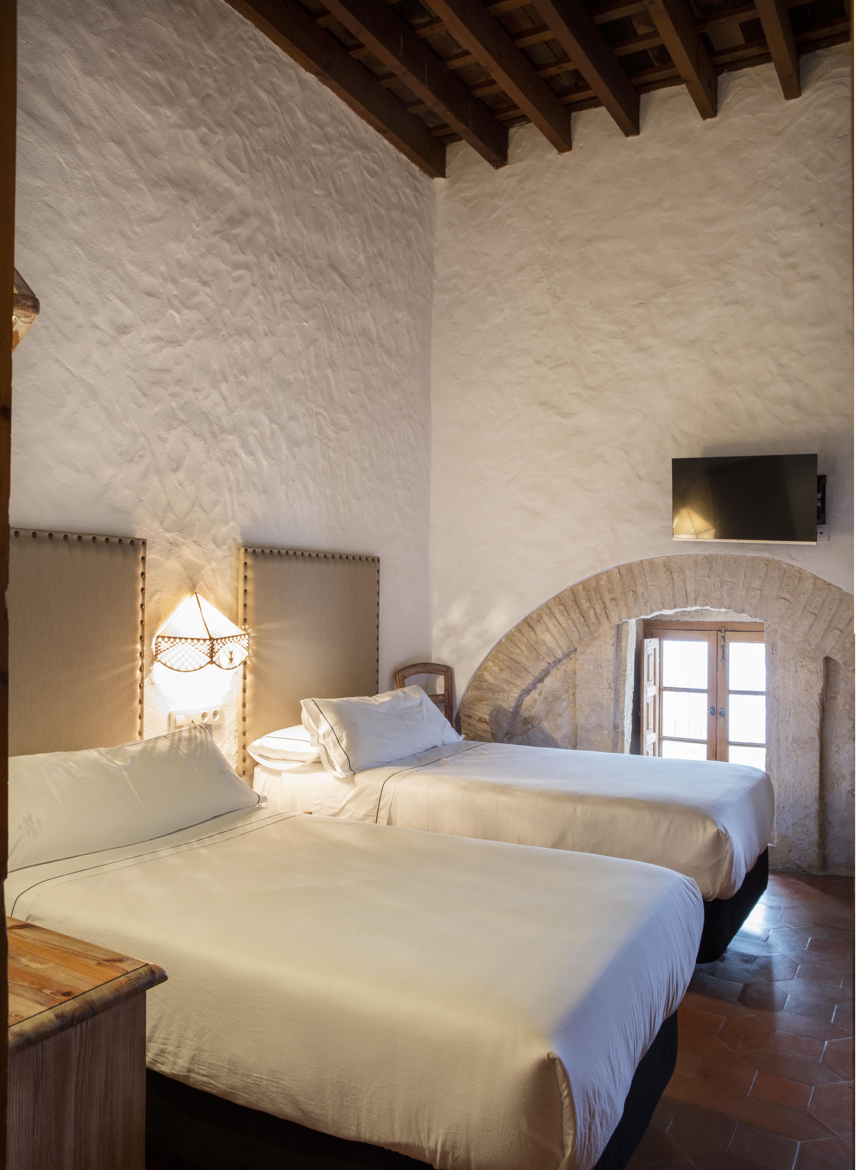 Un dormitorio con dos camas, techo de madera, pared de piedra y televisor fijado a la pared.