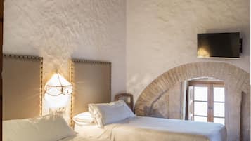 Un dormitorio con dos camas, techo de madera, pared de piedra y televisor fijado a la pared.