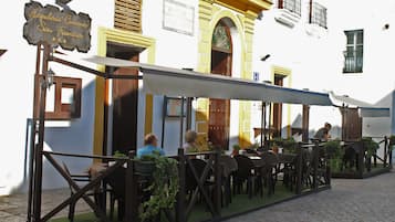 Een terras met tafels en stoelen, een bord met de tekst 'Hospedaria Convento San Francisco', en een gebouw met geel en wit gestucte muren.