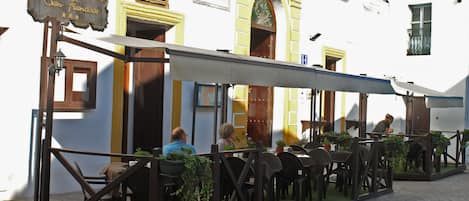 Un café al aire libre con mesas y sillas, un letrero que dice "Hospedaria Convento San Francisco" y un edificio de paredes amarillas y blancas.