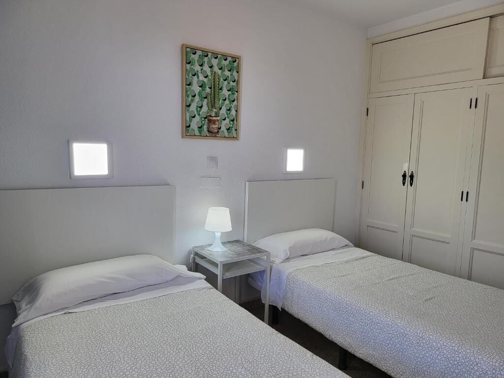 Una habitación con dos camas, una mesita de noche con lámpara, un cactus decorativo en la pared y un armario de dos puertas.
