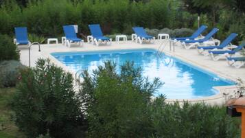 Une piscine entourée de chaises longues bleues et de tables blanches, avec une végétation luxuriante en arrière-plan.