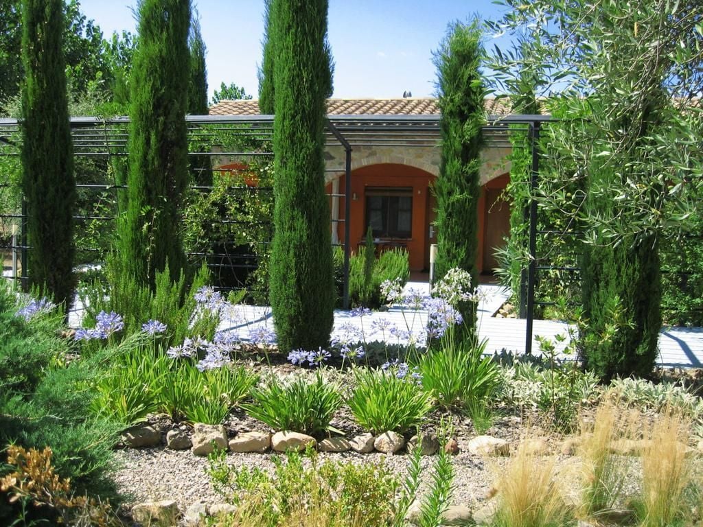 A building with a stone facade, an arched entrance, and a garden with various plants and flowers.