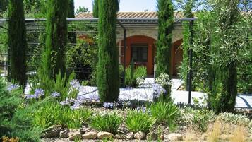 A building with a stone facade, an arched entrance, and a garden with various plants and flowers.