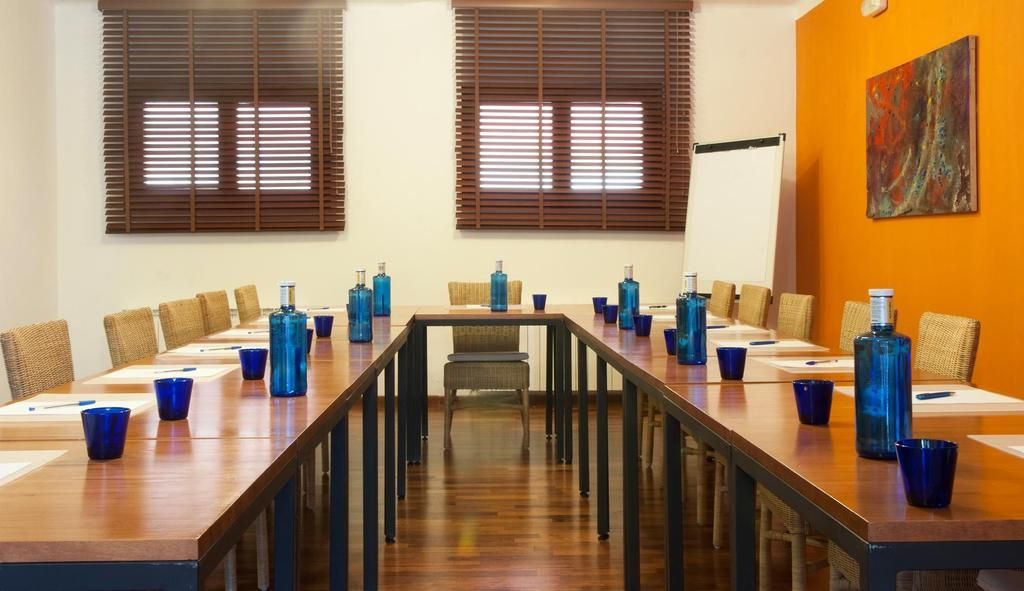Un salón de conferencias con una larga mesa, botellas de agua azules y sillas de mimbre.