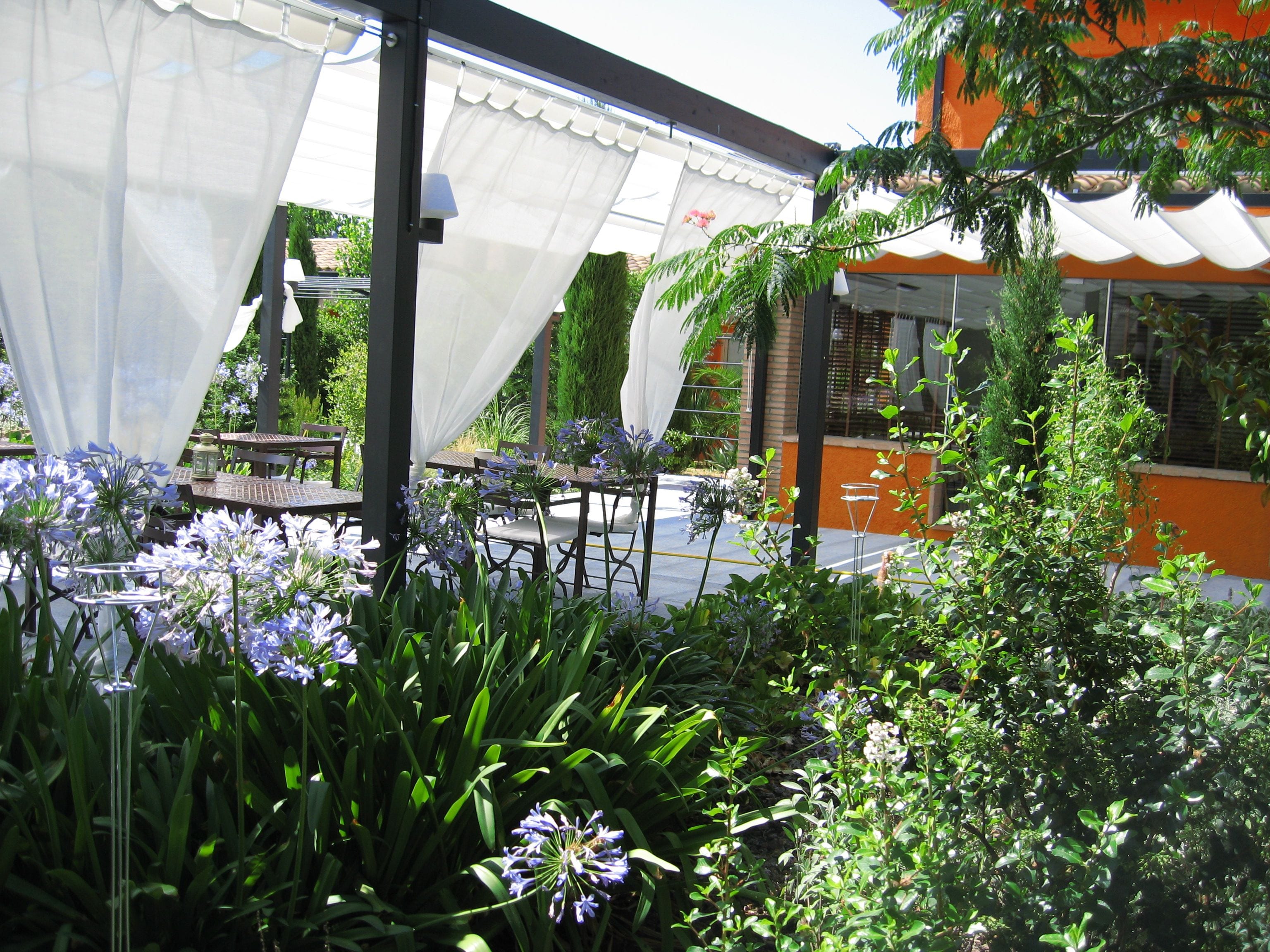 Un área de estar al aire libre con mesas y sillas, rodeada de exuberante vegetación y plantas florecientes.