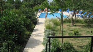 Ein Poolbereich mit einem klaren Weg zum Pool, umgeben von üppiger Vegetation und blauen Liegestühlen.