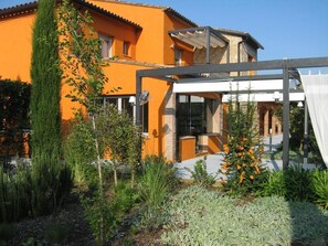 A modern house with a glass conservatory, surrounded by various plants and a garden. - Aatu (Forallac)