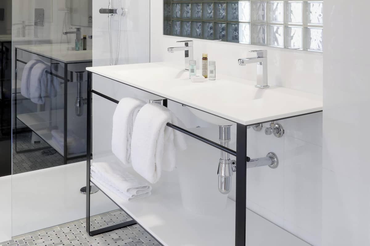 Une salle de bain moderne avec une douche à l’italienne en verre, un meuble-lavabo blanc doté d’un grand miroir et un mur recouvert de carreaux.