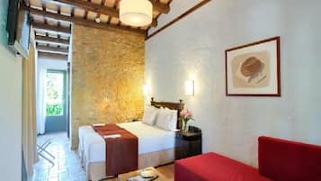 A room with a stone wall, a bed with white bedding, a red sofa, a wooden table, and a framed picture on the wall.
