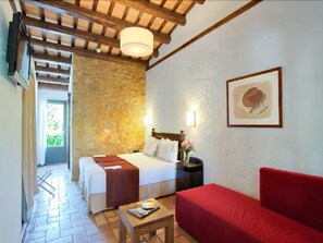 Ein Zimmer mit einer Steinwand, einem Bett mit weißer Bettwäsche, einem roten Sofa, einem Holztisch und einem gerahmten Bild an der Wand.