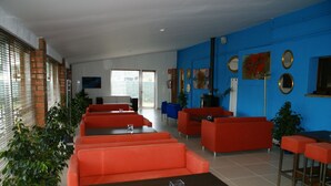 Een modern interieur met rode banken en tafels, een blauwe accentmuur en een groot raam met zonwering.