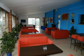 Un intérieur moderne avec des canapés et des tables rouges, un mur d’accent bleu et une grande fenêtre avec des stores.