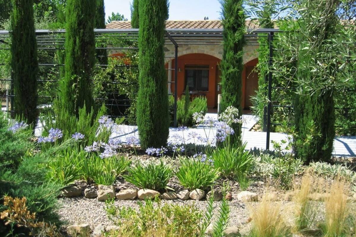 Un jardin où l’on trouve différentes espèces de plantes et un bâtiment doté d’un toit recouvert de tuiles et d’une entrée en arc de cercle.