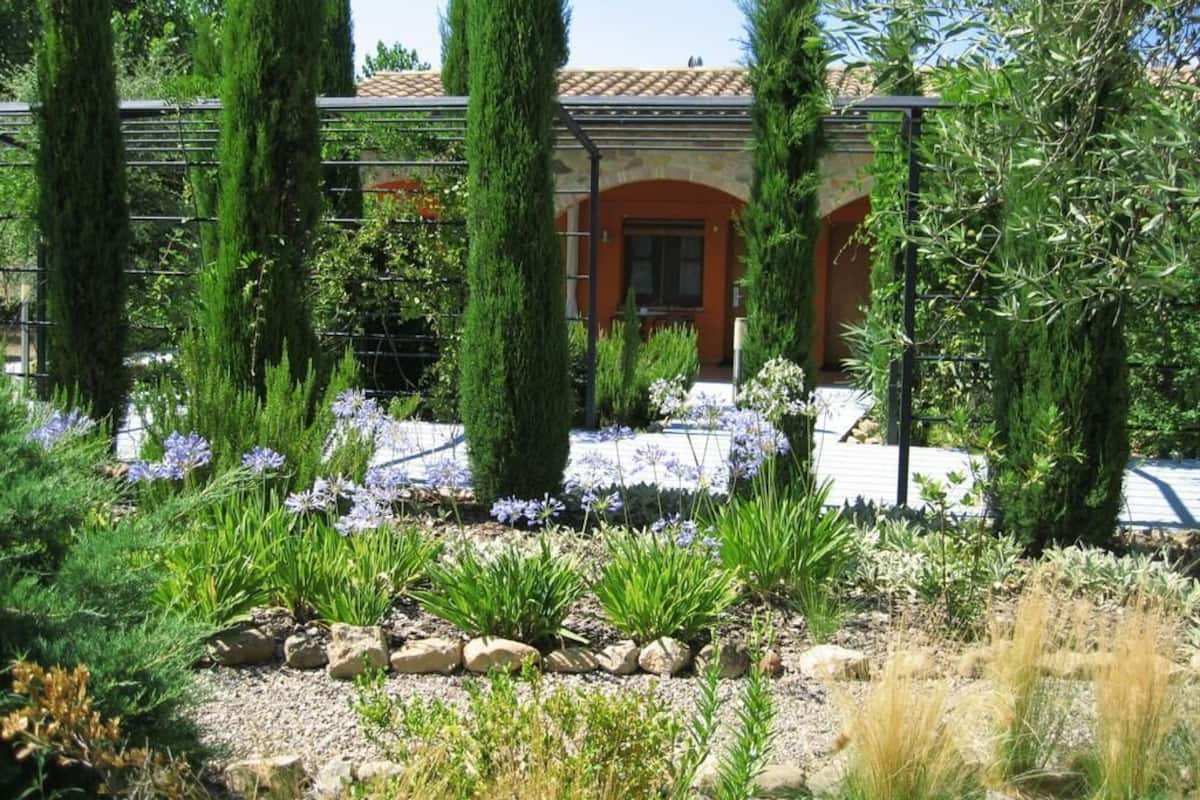 Un edificio con fachada de piedra, tejado de tejas y un jardín con diversas plantas y flores.