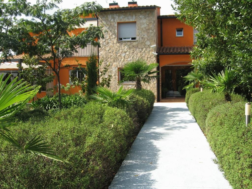 Un camino que lleva a un edificio con paredes de piedra y color naranja, rodeado de abundante vegetación.